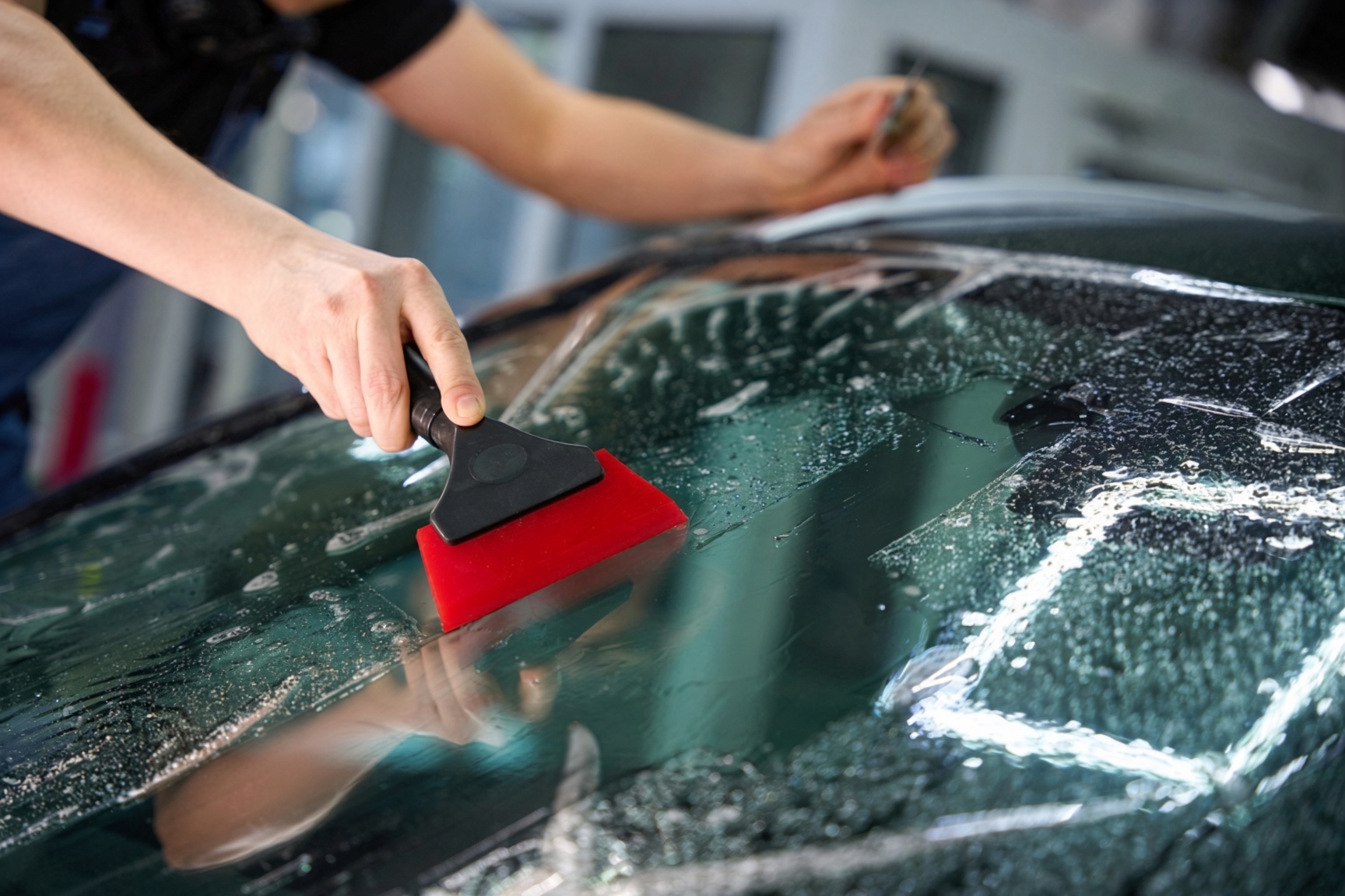 Technician applying windscreen protection film with a squeegee